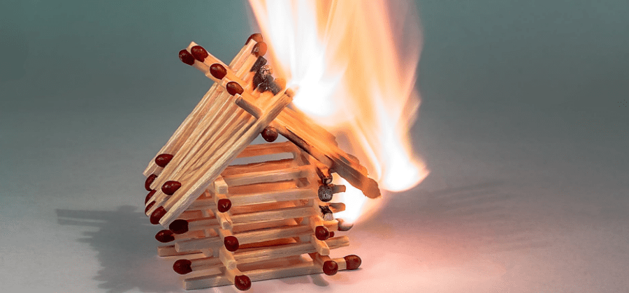 House model made out of matchsticks partially lit with fire