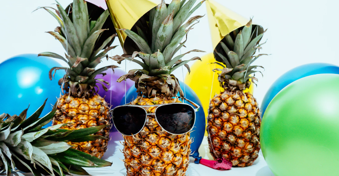 three pineapples dressed with party hats and sunglasses