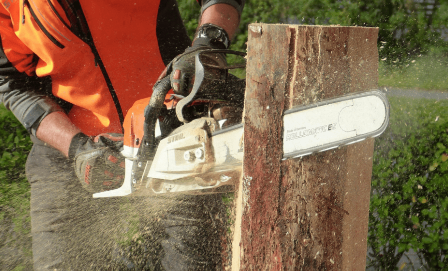A male worker using a chainsaw to cut a tree trunk