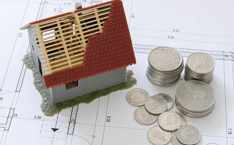 model of a damaged house and coins next to it