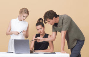 A man pointing at something at a laptop to two women