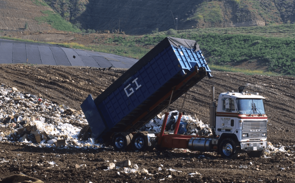 A dump truck unloading at a landfill of trash