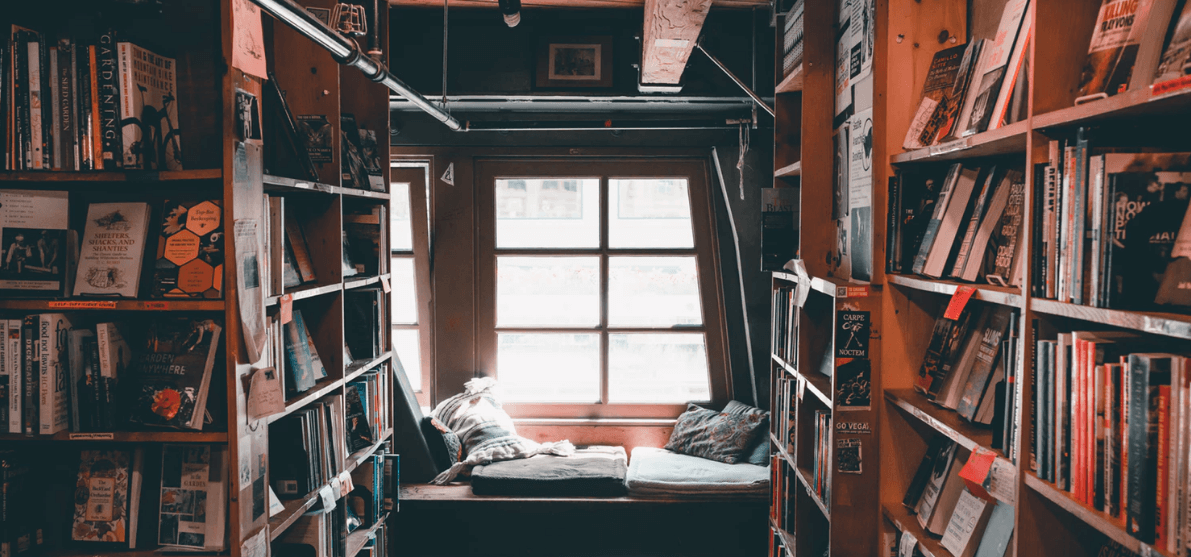 Shelves of books in a library with a cozy nook and windows
