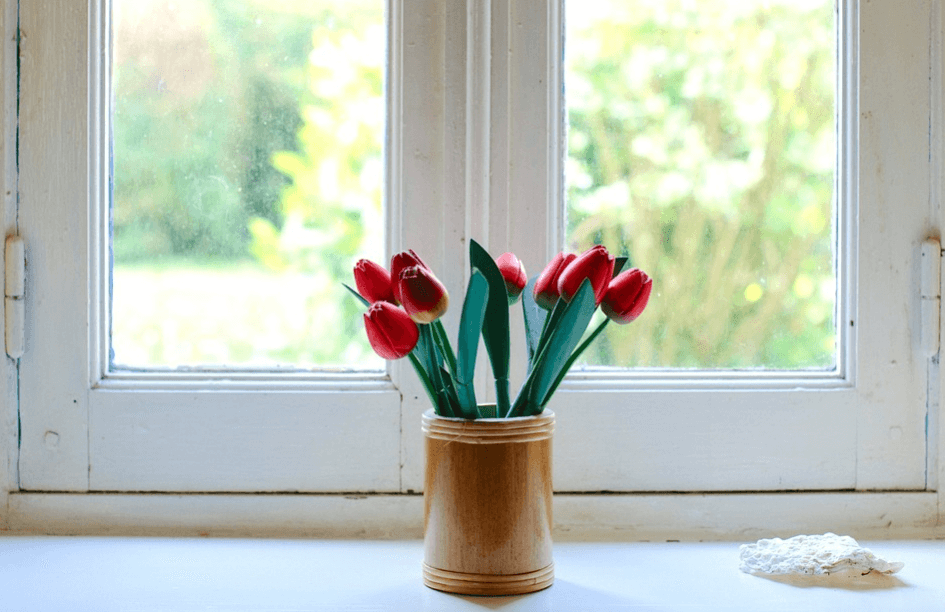 A vase of fresh tulip flowers in front of a window