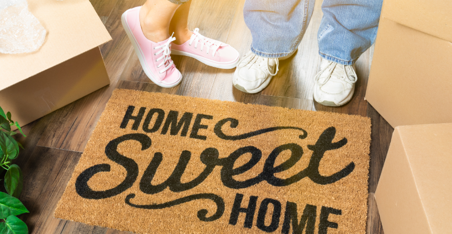 Photo of couple's feet standing next to welcome mat "Home Sweet Home"